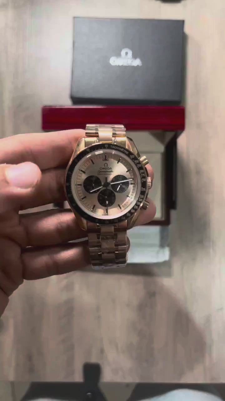 Reloj cronógrafo en tono oro rosa con bisel negro taquimétrico, esfera champagne con tres subesferas negras y brazalete de acero, sostenido en la mano frente a una caja roja
