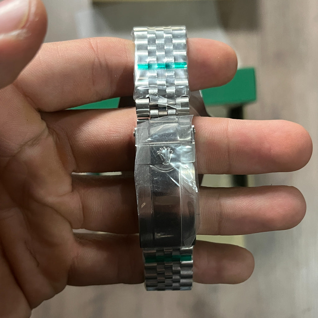Reloj de acero con bisel azul y rojo, esfera negra con fecha y brazalete de cinco eslabones, sostenido en la mano