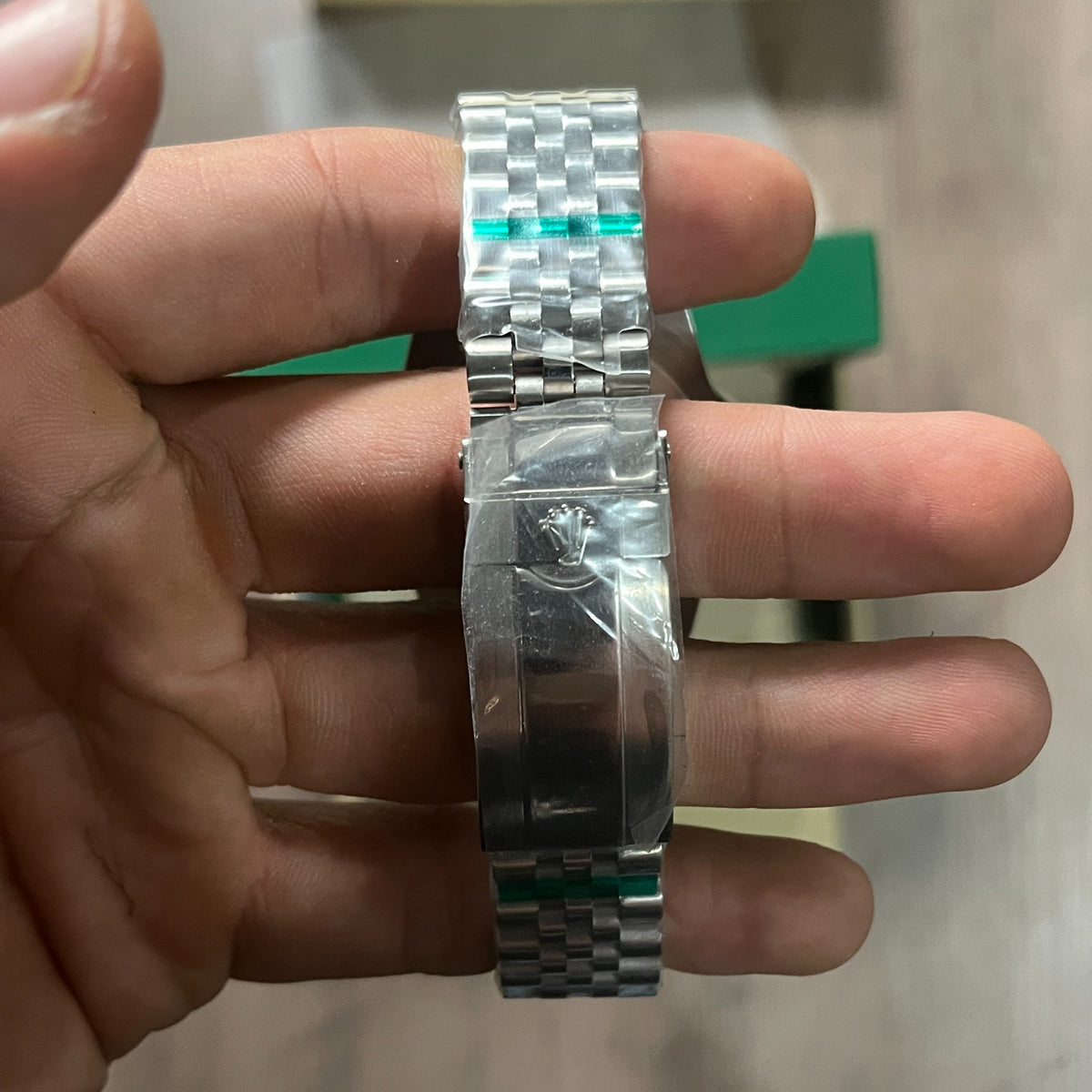 Reloj de acero con bisel azul y rojo, esfera negra con fecha y brazalete de cinco eslabones, sostenido en la mano