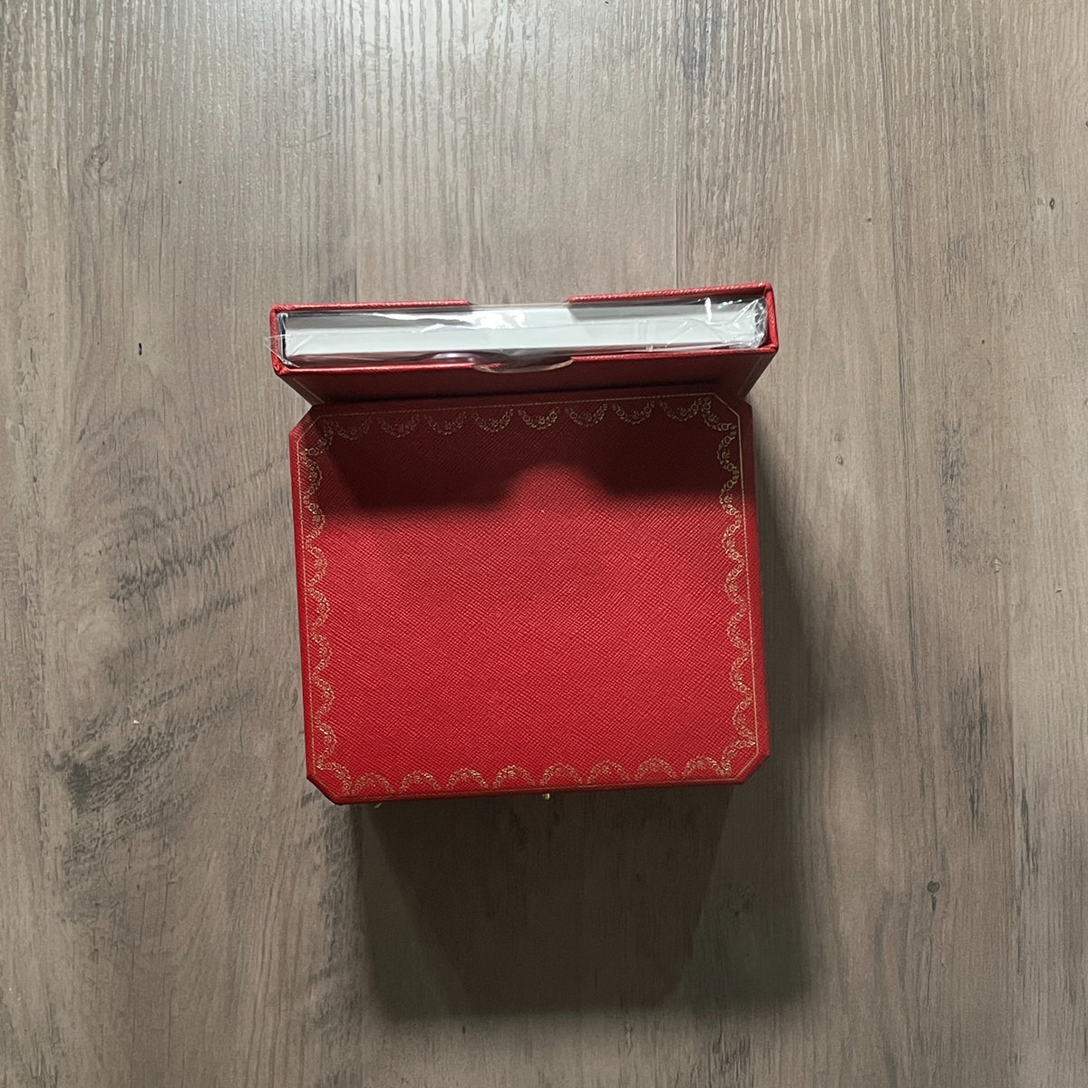 Reloj cuadrado de acero con esfera blanca, números romanos y manecillas azules, sostenido en la mano frente a una caja roja